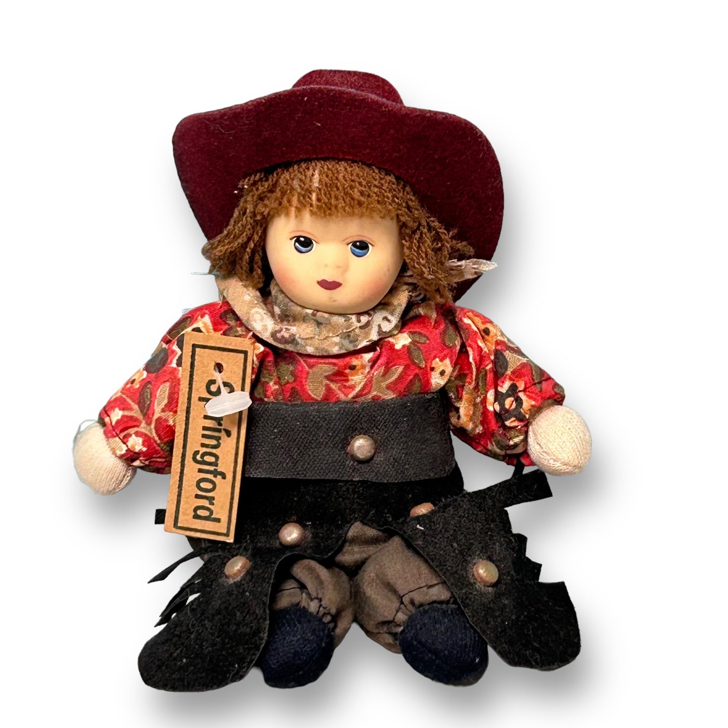 A vintage Springford porcelain cowboy doll with a red hat and a floral shirt, sitting against a white background.