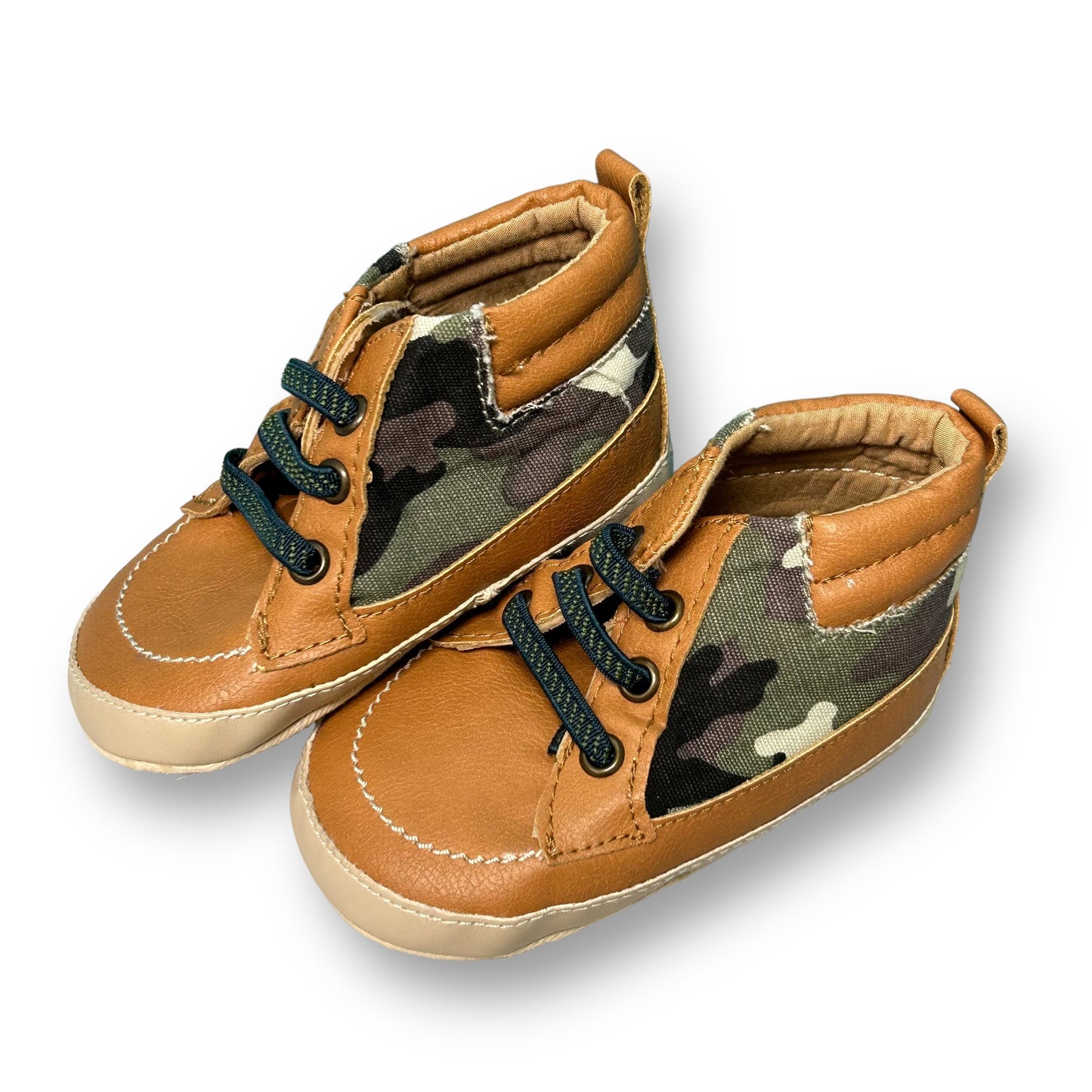 A pair of tan slide-on baby shoes with a camouflage pattern.