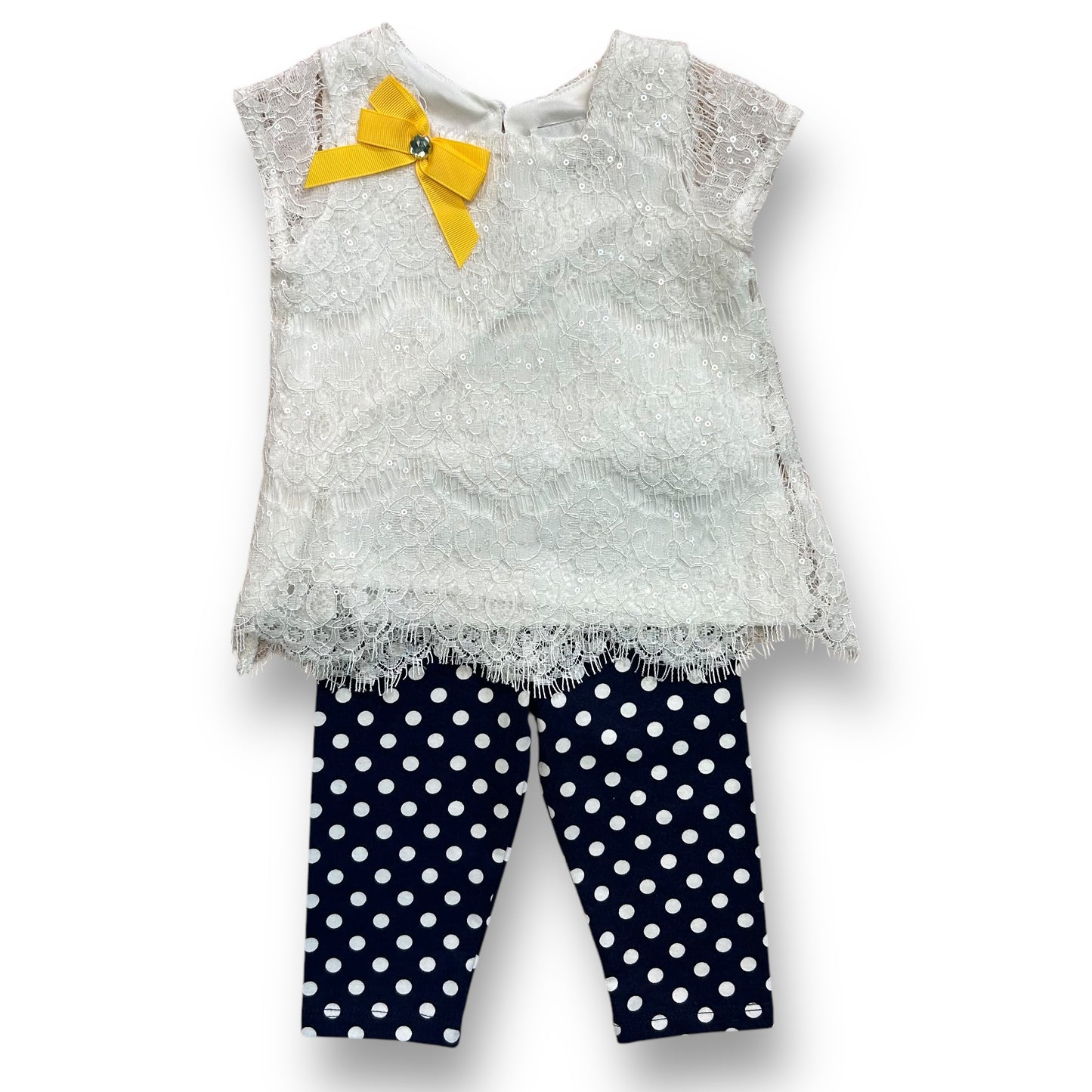 A white sequin blouse with a yellow bow and lace details, and dark blue leggings with a polka dot pattern.