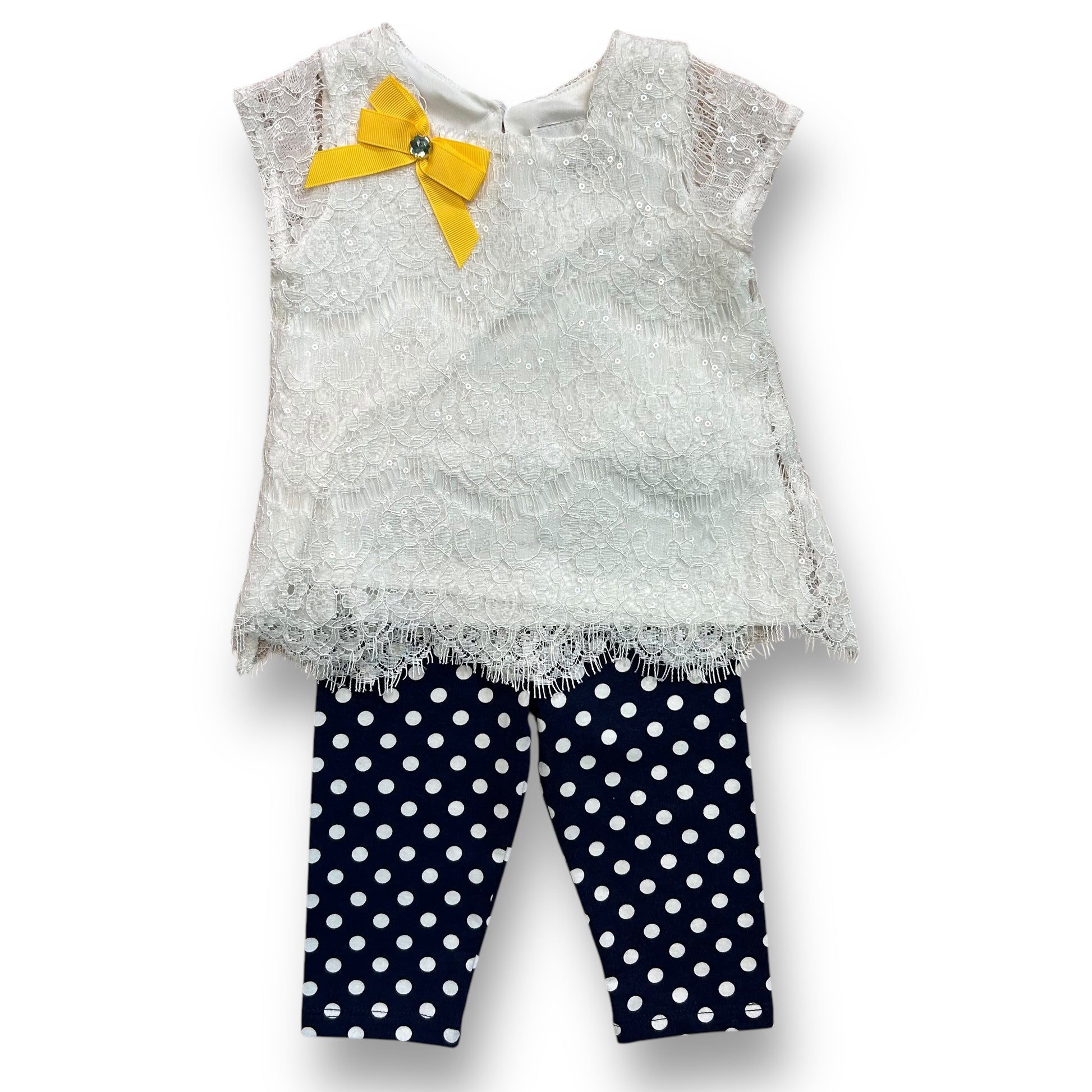 A white sequin blouse with a yellow bow and lace details, and dark blue leggings with a polka dot pattern.