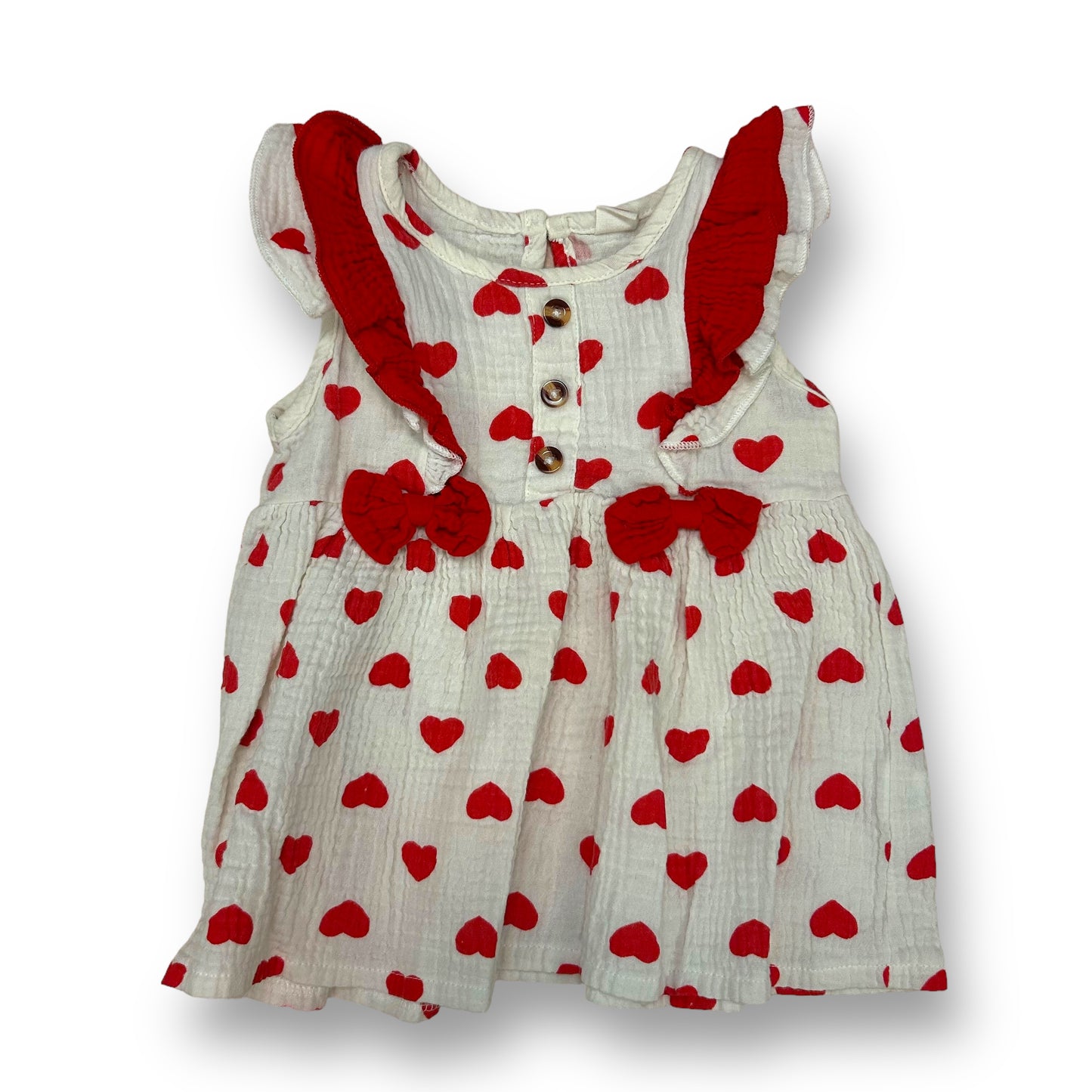 A sleeveless, red and cream colored dress with a heart pattern, featuring bows and a ruffled detail.
