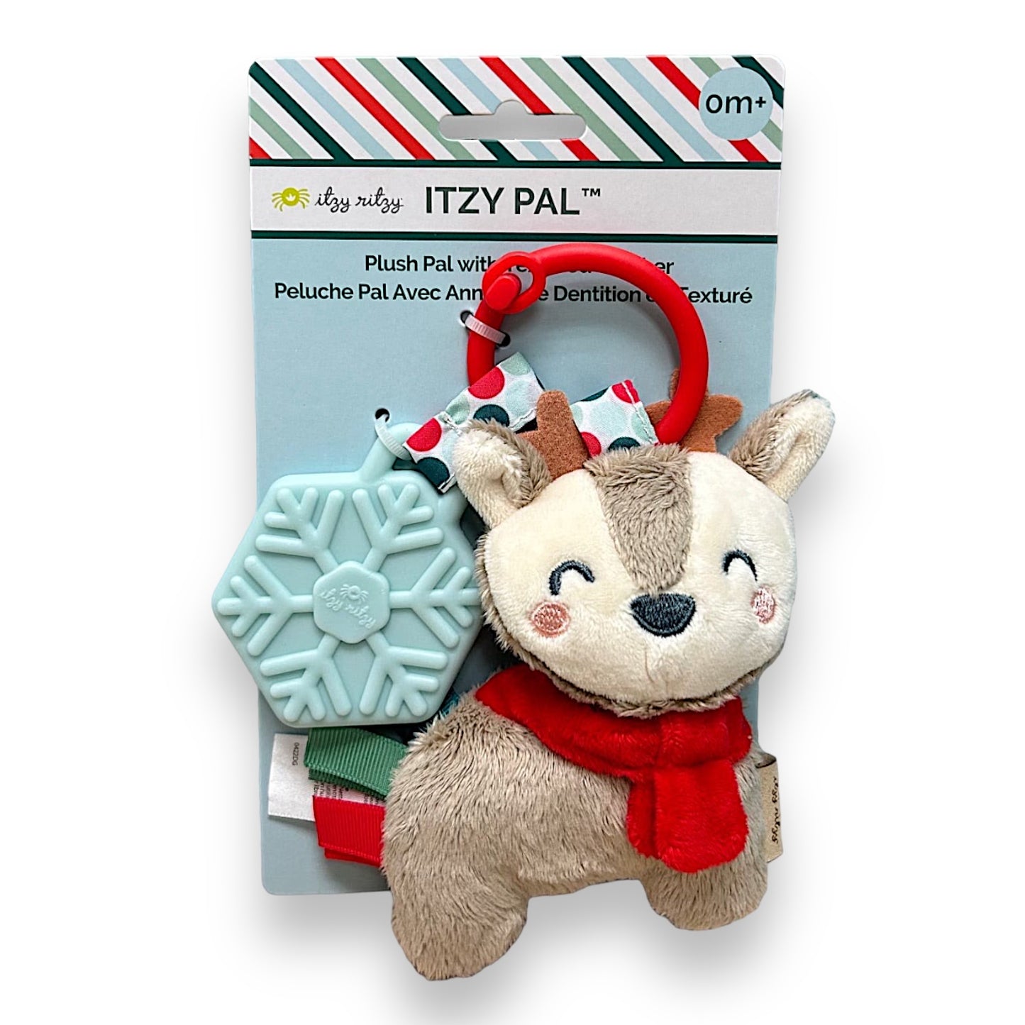 A packaged Itzy Ritzy Reindeer Holiday Plush & Teether Pal. The plush toy is beige with a red scarf and has a teether attached to it, presented in a Christmas-themed card packaging.