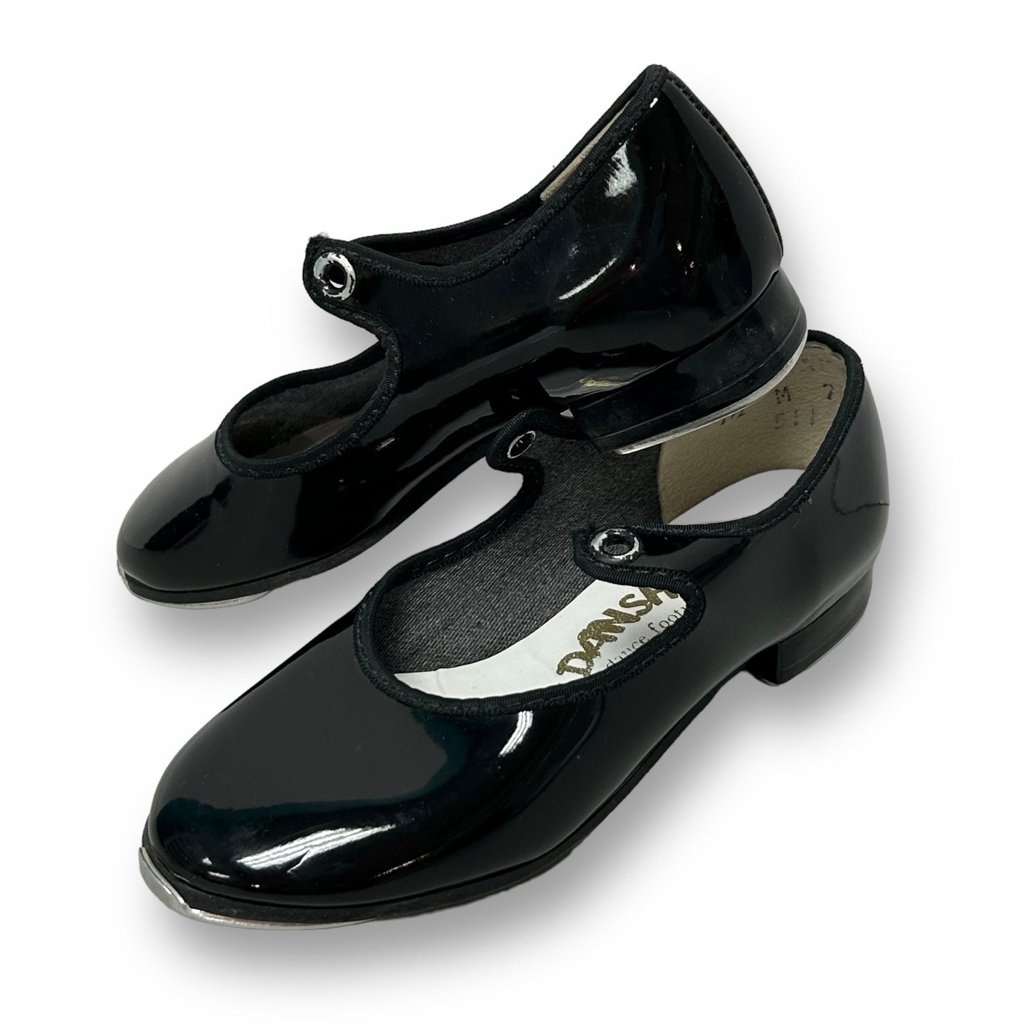A pair of black patent leather toddler girl tap shoes with the brand name 'Danshuz' visible on one of the shoes.