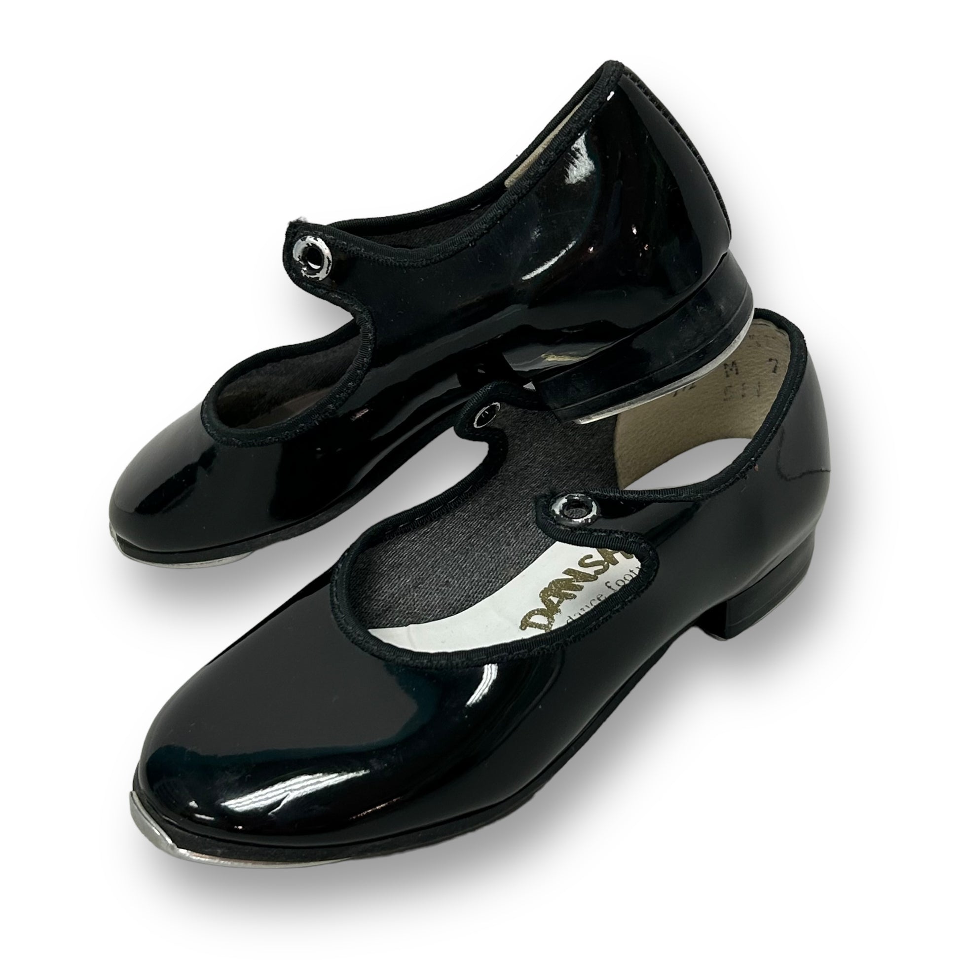 A pair of black patent leather toddler girl tap shoes with the brand name 'Danshuz' visible on one of the shoes.
