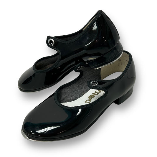 A pair of black patent leather toddler girl tap shoes with the brand name 'Danshuz' visible on one of the shoes.