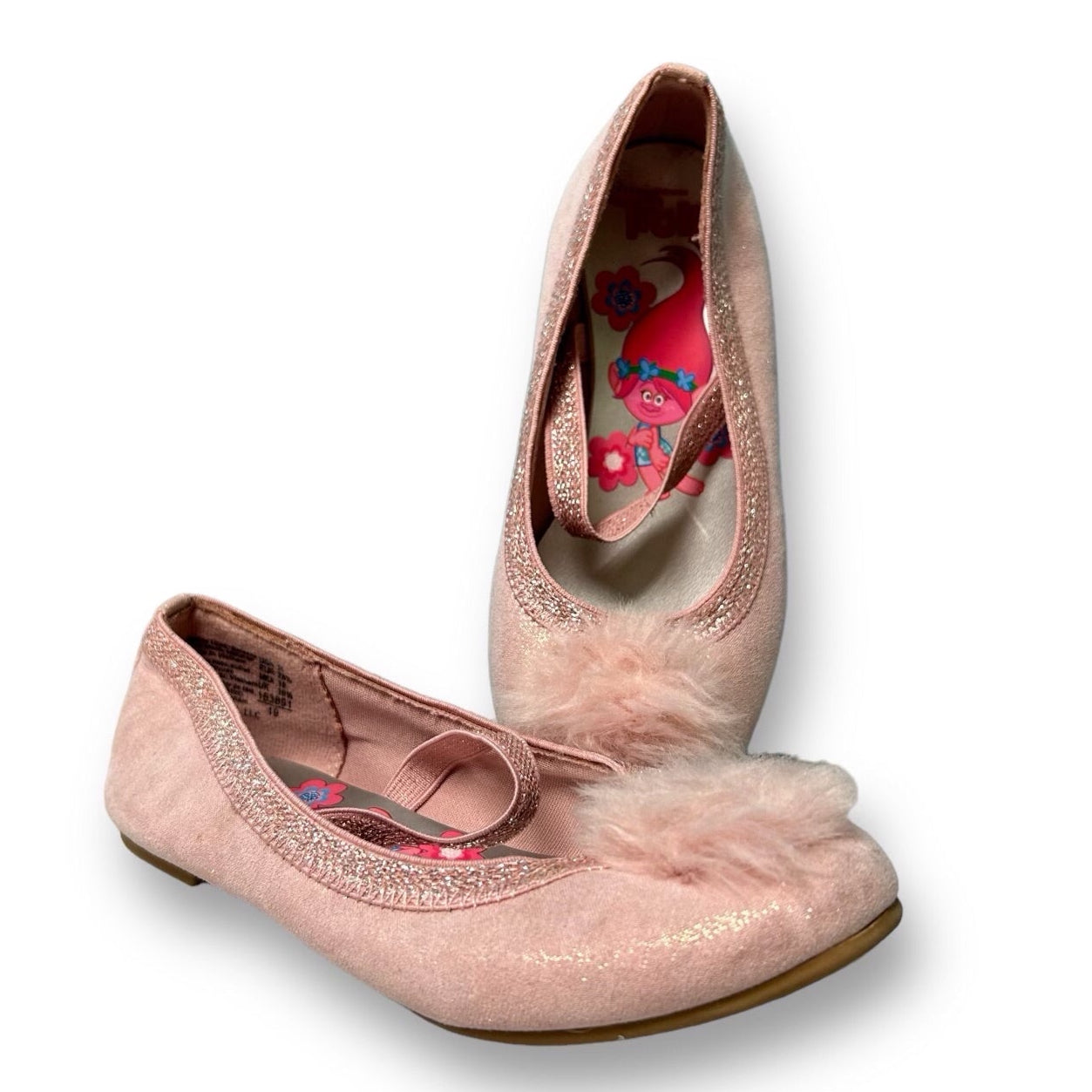A pair of pink baby girl shoes with pom poms and floral patterns on a white background.