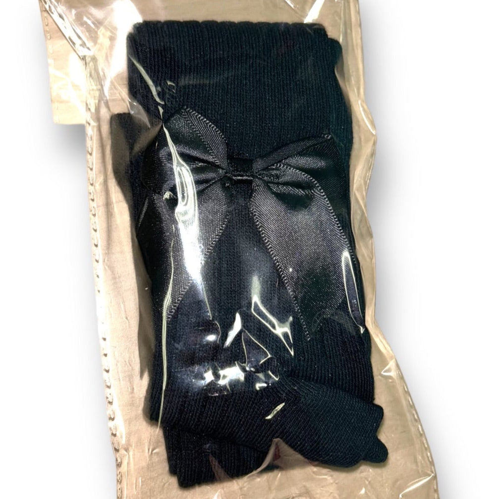 Baby girl black ribbed tights with bow accents, packaged in a clear plastic bag.