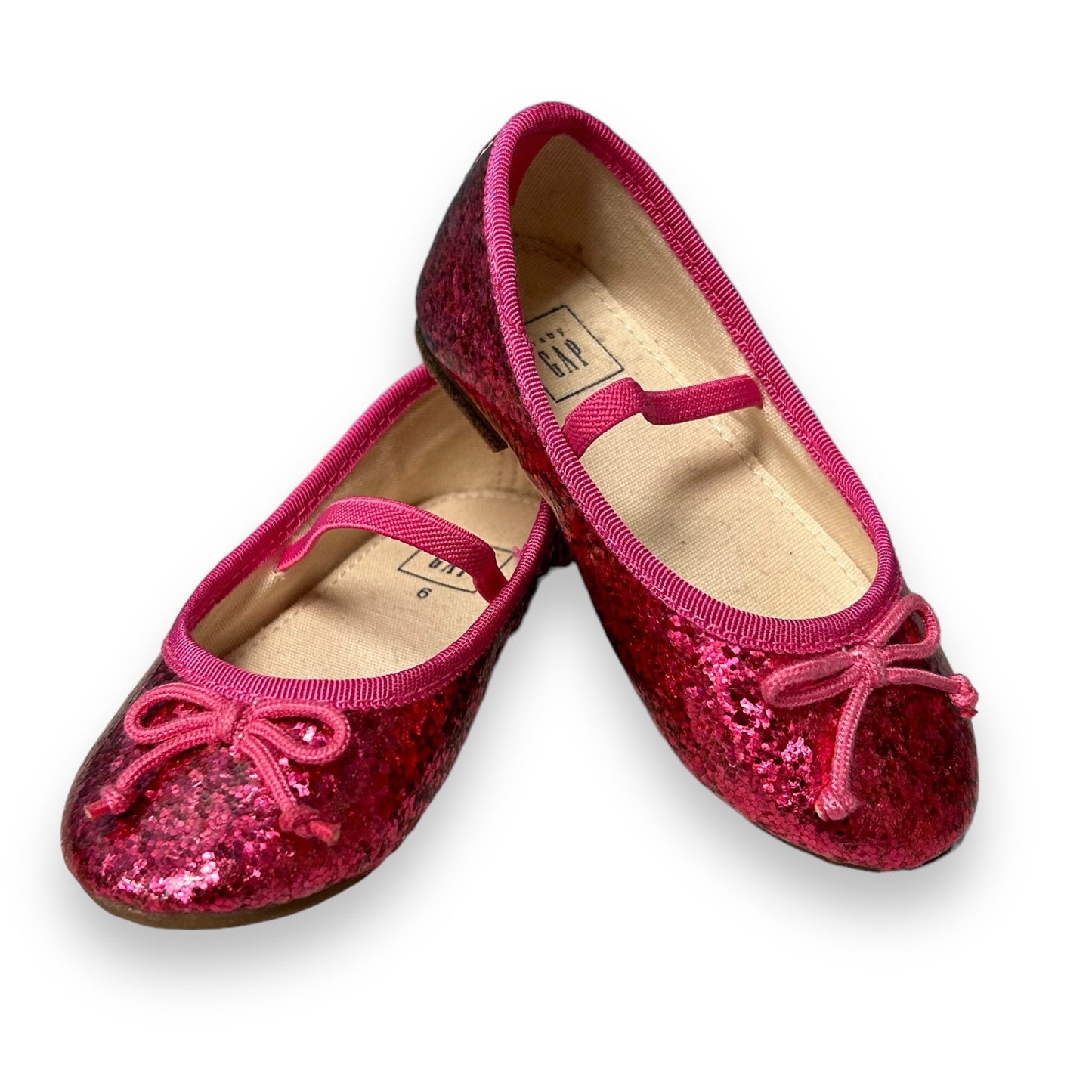 A pair of shimmery pink toddler girl casual dress shoes with a bow detail on a white background.