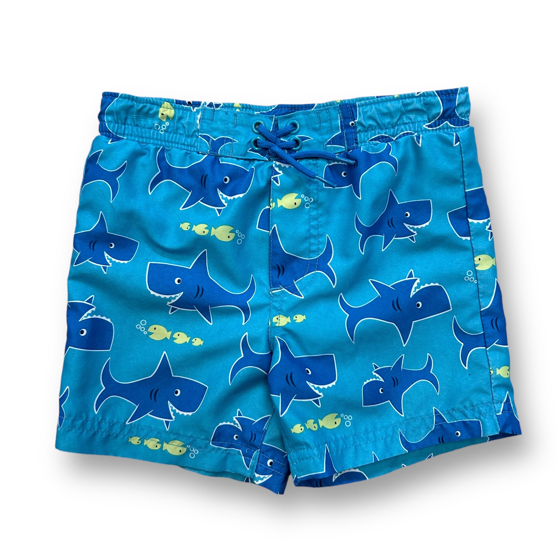 A pair of blue swim trunks with a shark print design, featuring a drawstring waist and a brand label at the bottom.