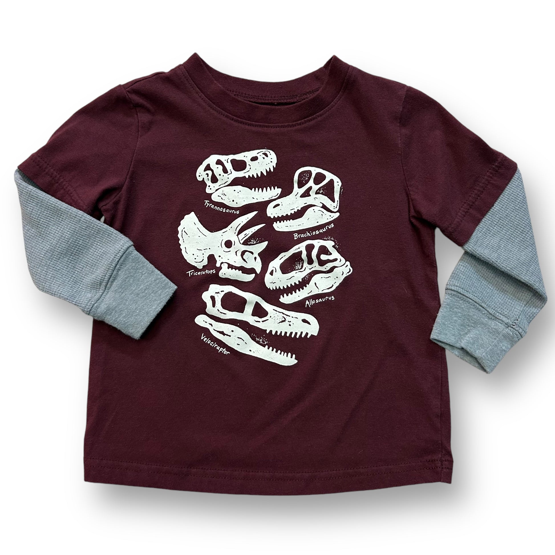 A maroon long-sleeve thermal tee with a pattern of dinosaurs on it, designed for a toddler.