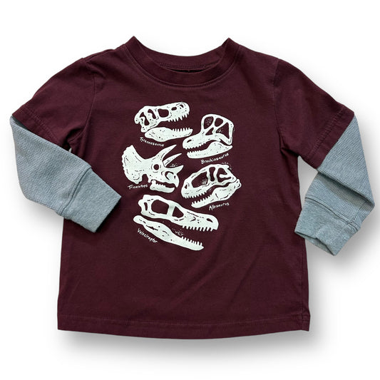 A maroon long-sleeve thermal tee with a pattern of dinosaurs on it, designed for a toddler.