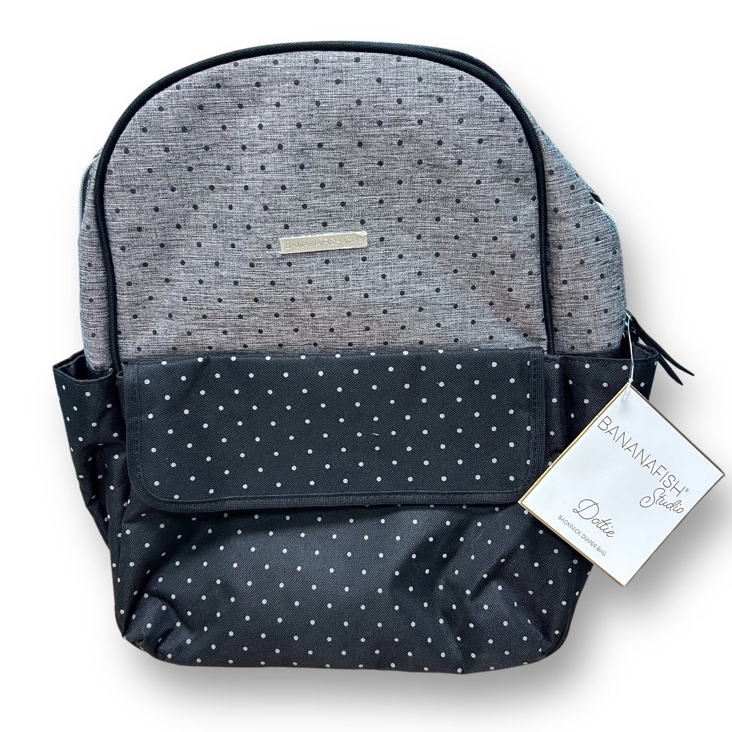 A gray and black dotted Bananafish Studio backpack diaper bag with a brand tag attached to it.
